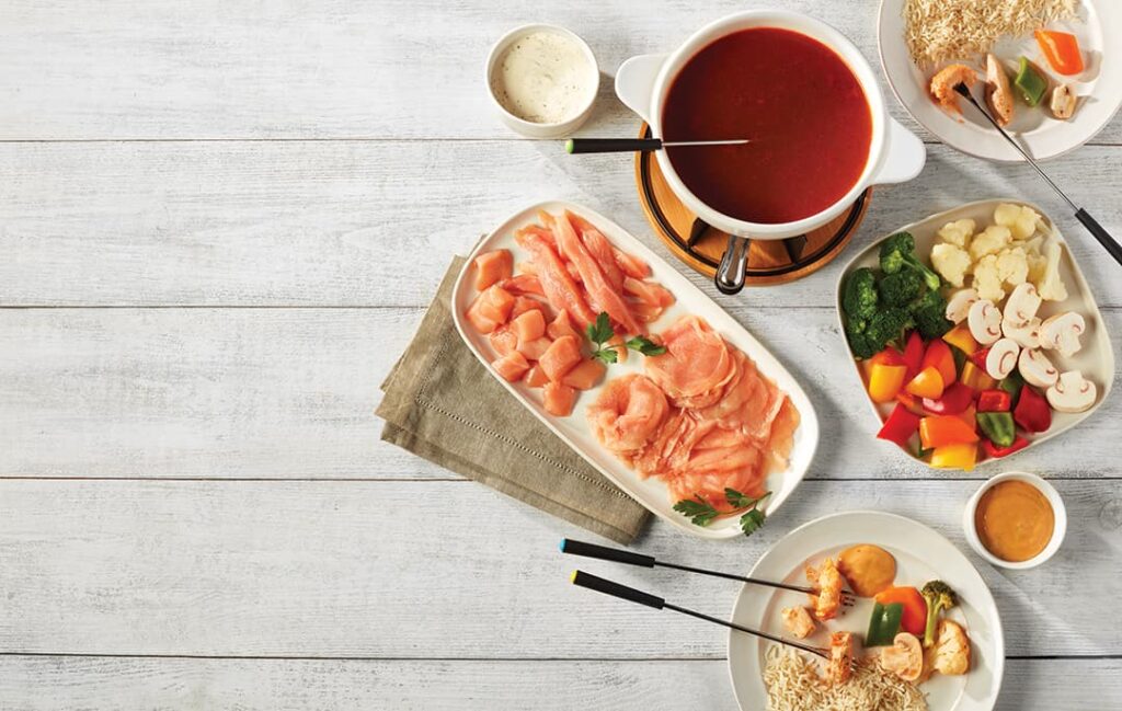 Ferme des Voltigeurs fondue chinoise au poulet de grain sur table avec bouillon, légumes et accompagnements.