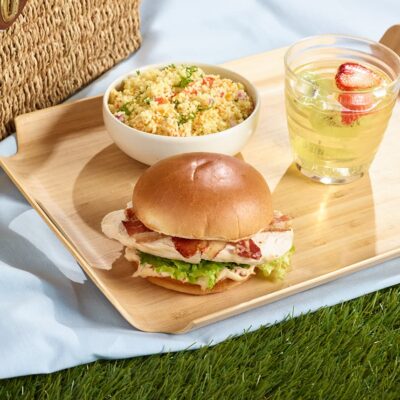 Le club césar de chez Ferme des Voltigeurs avec salade d'accompagnement dans une ambiance pic-nic. / Ferme des Voltigeurs Caesar Club Sandwich with Side Salad in a Picnic-Inspired Setting.
