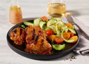 Grain-fed boneless chicken thighs Ferme des Voltigeurs with side dishes and on a black plate.