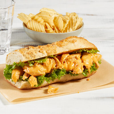 Sandwich au poulet chipotle de Ferme des Voltigeurs, photo ambiance sur table grise et accompagnement de chips. / Ferme des Voltigeurs Chipotle Chicken Sandwich, lifestyle photo on a gray table with a side of potato chips.