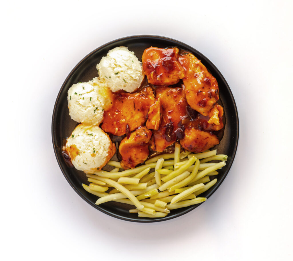Repas de poulet canneberges de Ferme des Voltigeurs. Assiette noire sur fond blanc. / Ferme des Voltigeurs Cranberry Chicken Meal. Black Plate on a White Background.
