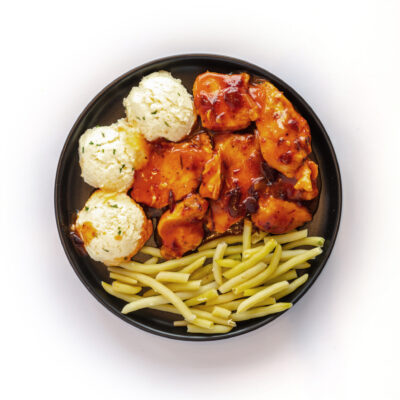 Repas de poulet canneberges de Ferme des Voltigeurs. Assiette noire sur fond blanc. / Ferme des Voltigeurs Cranberry Chicken Meal. Black Plate on a White Background.