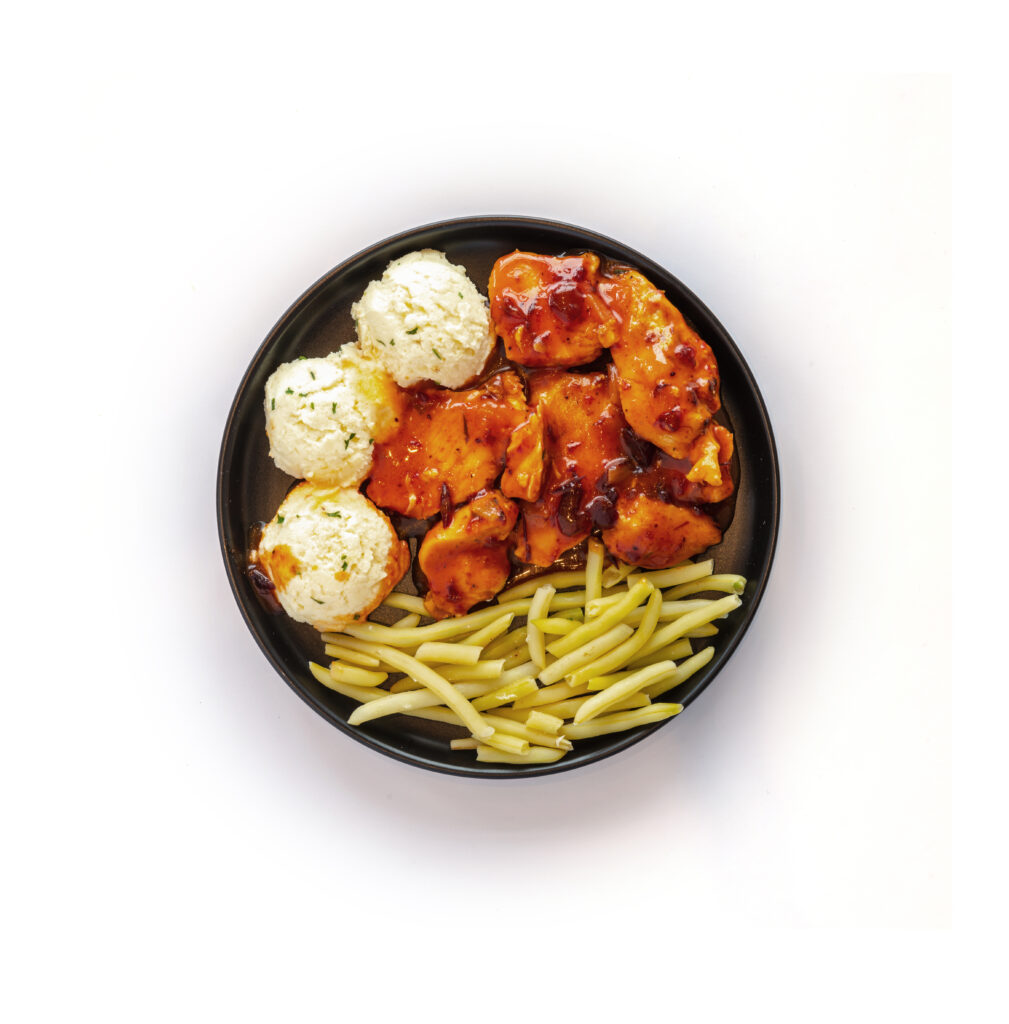 Poulet aux canneberges dans assiette noire sur fond blanc de Ferme des Voltigeurs, format carrousel. / Cranberry Chicken from Ferme des Voltigeurs, served on a black plate against a white background, carousel format.